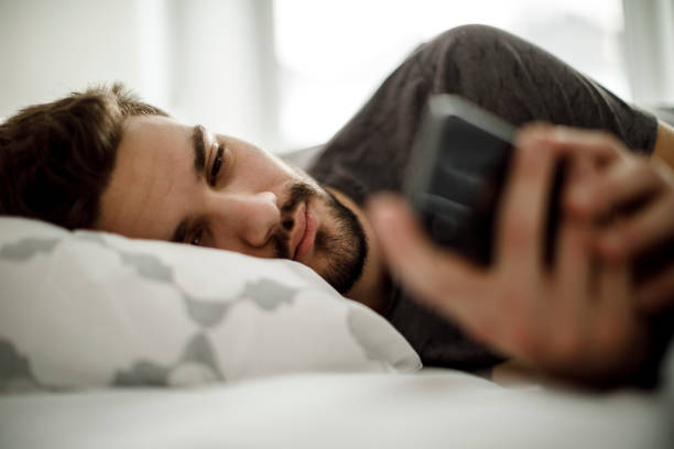 Sad man in bed text messaging Sad man in bed text messaging waking up photos stock pictures, royalty-free photos & images