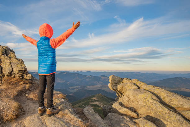 маленький мальчик турист стоял с поднятыми руками в горах, наслаждаясь видом на удивительный горный пейзаж на закате. - rock human hand human arm climbing стоковые фото и изображения