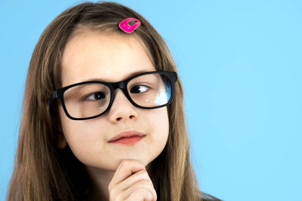 fermez-vous vers le haut du portrait d’une fille d’école d’enfant aux yeux croisés utilisant des lunettes regardantes isolées sur le fond bleu. - cross eyed photos photos et images de collection