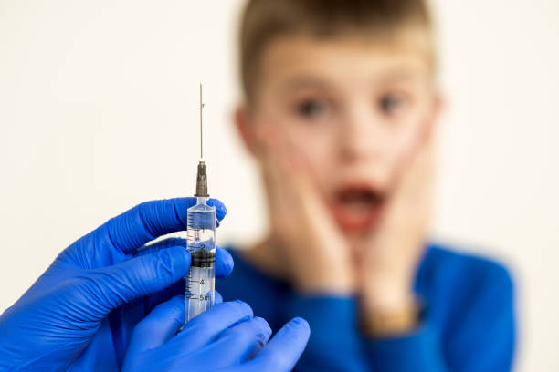두려워하는 아이 소년에게 주사기로 예방 접종 주사를 준비하는 의사. 학교 개념에서 아이들의 예방 접종. - injecting syringe spooky male 뉴스 사진 이미지