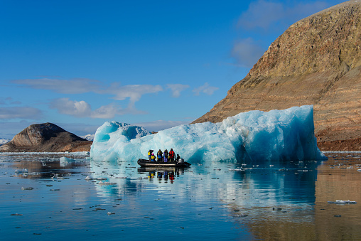 Landscape with iceberg in Greenland at summer time. Sunny weather. Inflatable boat with tourists.