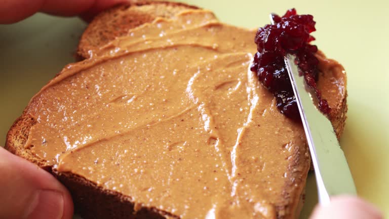 Spreading fruit jam on toast with peanut butter