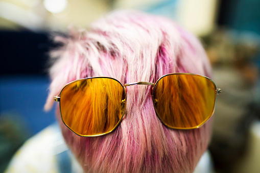 Yellow sunglasses on the top of the pink dyed hair of a young woman