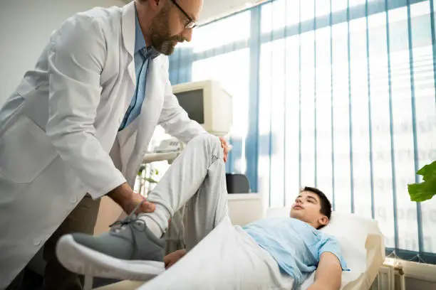 A mature doctor examines the mobility and 
condition of a boy's knee.