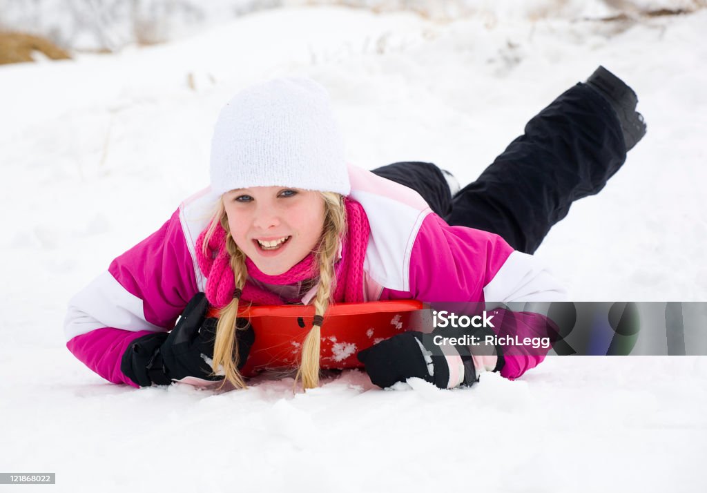 Winter Play A young blond girl sledding on a snowy hill. 12-13 Years Stock Photo