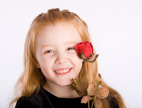 A happy young girl holding a single red rose.