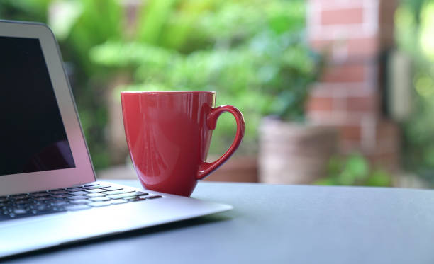 istock Computer laptop and coffee in red cup on top of table. Garden view. 1218686830