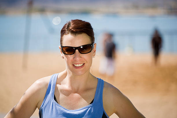 A woman in fitness clothes standing on a beach volleyball court.