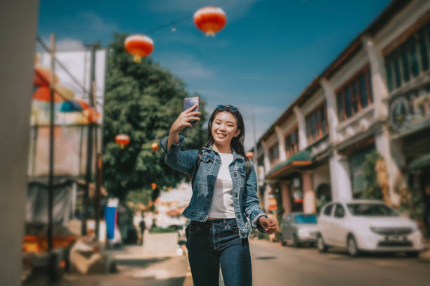 una giovane turista cinese asiatica a penang, malesia, sud-est asiatico scattando foto per strada con il suo cellulare - asian country foto e immagini stock