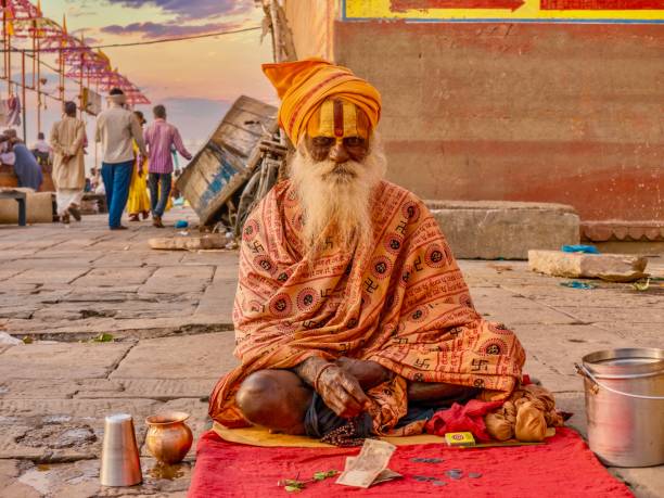 indyjski sadhu siedzi skrzyżowane nogi, zbierając datki w pobliżu ghats varanasi, indie. - swastyka hinduska zdjęcia i obrazy z banku zdjęć