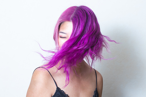 A Korean woman with pink and purple hair swings her hair in front of a white background