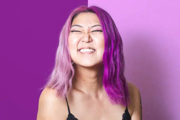 A Korean woman with pink and purple hair grins at the camera