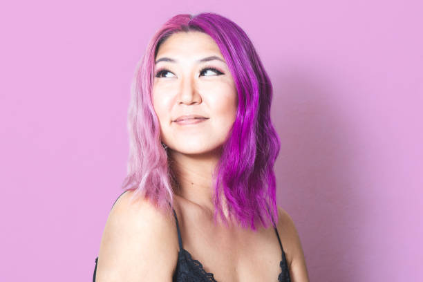 Pink and Purple Hair Against Matching Pink Background A Korean woman with pink and purple hair against a pink background looks off-camera with a slight smile purple hair stock pictures, royalty-free photos & images