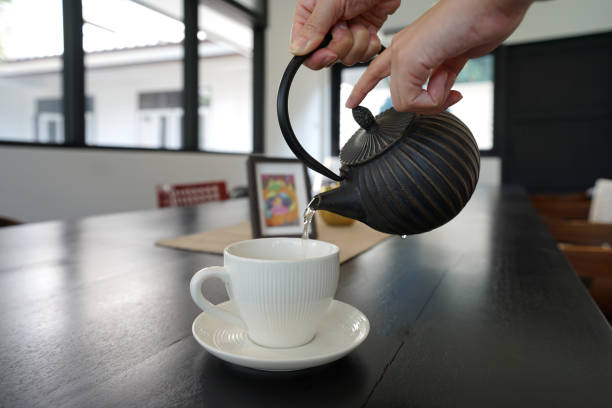 istock Human hands pouring the tea from black teapot into white porcelain ceramic tea cup 1218695435