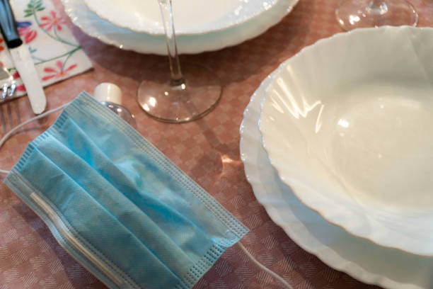 istock Table set up with dinnerware and silverware, ready for a meal. with surgical mask. 1218699213