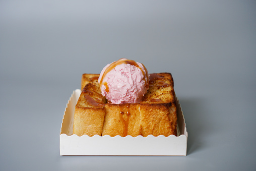 a square toast baking with butter and topped with strawberry ice cream and caramel sauce, grey background, centre.