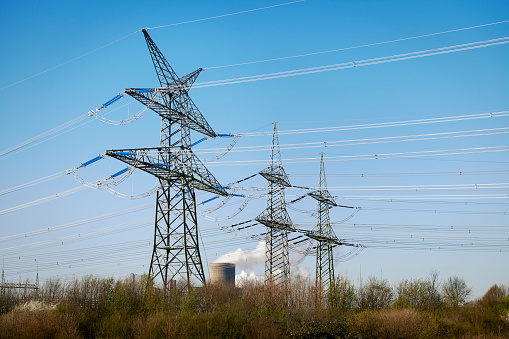 Three electricity pylons in front of a coal-fired power plant with pollution.