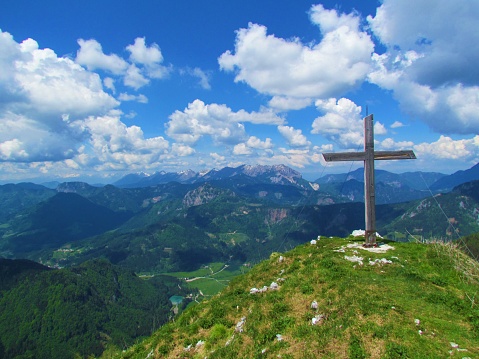 Young woman on top of a mountain (Moerzelspitze) holding the summit cross looking at Lake of Constance in the background