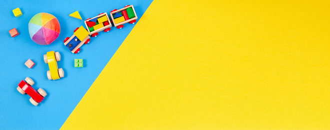Baby kids toys banner background. Wooden train, toy car, colorful blocks on blue and yellow background. Top view, flat lay