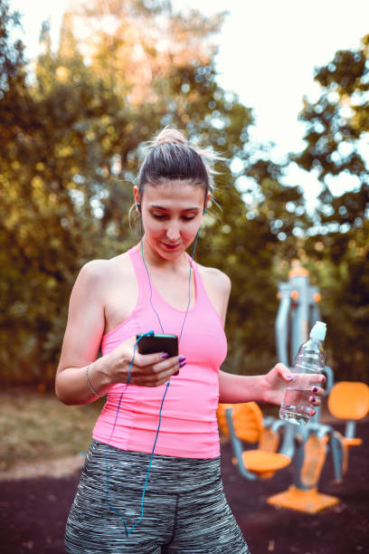 istock Female Athlete Changing Song On Smartphone While Hydrating After Workout 1218714512