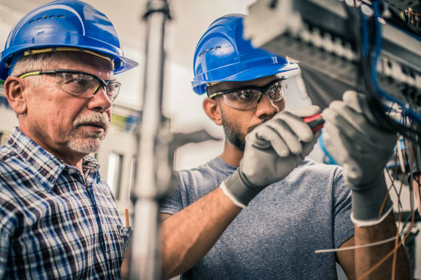 Male apprentice connecting wires in the distribution board Young male apprentice connecting the wires in the distribution board under supervision of a senior electrician. t shirt caucasian photography color image stock pictures, royalty-free photos & images