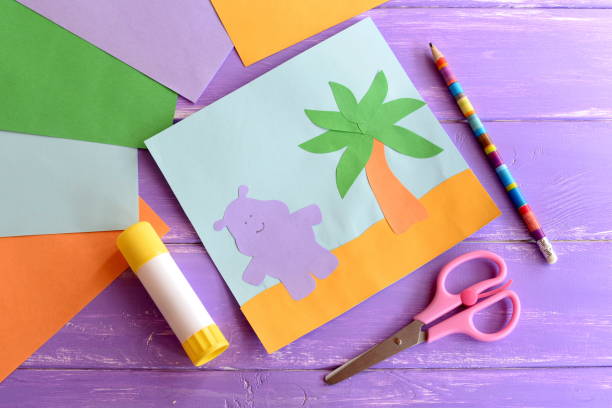Hippopotamus craft for kids. Hippopotamus craft diy. Hippopotamus craft preschool. Hippopotamus art kids hippo crafts. Hippopotamus paper craft. Hippopotamus diy. Summer card ideas paper crafts. Card step by step paper crafts. Card making step by step paper crafts. Paper palm tree diy. DIY palm tree leaves paper. Hippo paper craft for kids. DIY hippo paper. Card making workshop. Paper workshop kids artesanía preescolar de hipopótamo y palmeras. tarjeta de papel de verano, tijeras, palo de pegamento, hojas de papel de colores sobre un fondo de madera. animales artesanías arte idea proyecto para los niños. artesanías fáciles para que los niños h