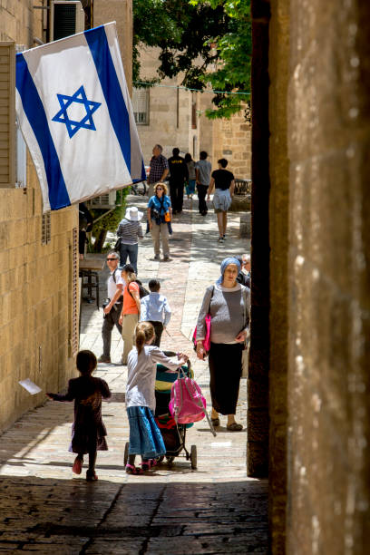 menschen, die auf einer schmalen straße der jerusalemer altstadt spazieren gehen, die sonne scheint durch die israelische flagge mit davidstern, der an einem fenster in jerusalem, israel, hängt. - israel judaism israeli flag flag stock-fotos und bilder