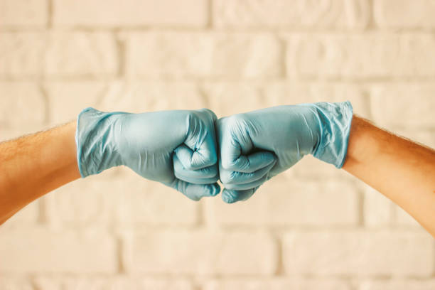 Men bumping fists in protective medical gloves