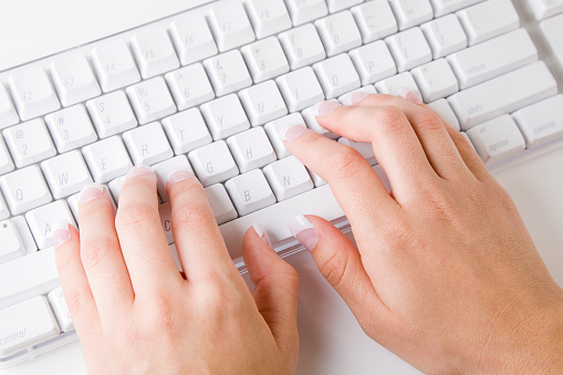 A top-down view of a woman's hands typing on a computer keyboard.