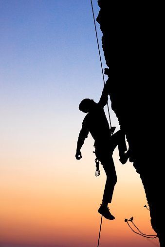 Male rock climbing pulling up, doing next step reaching top. Side view.