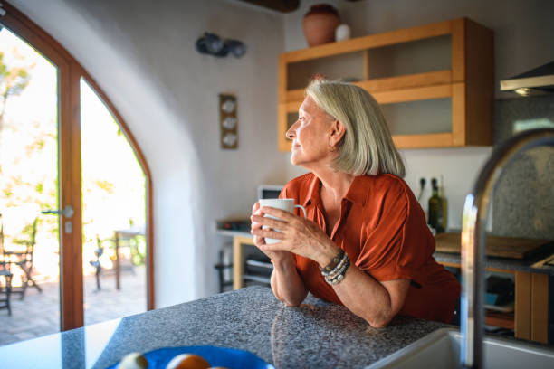 femme aînée contemplative avec le café regardant dehors la fenêtre - 3517 photos et images de collection