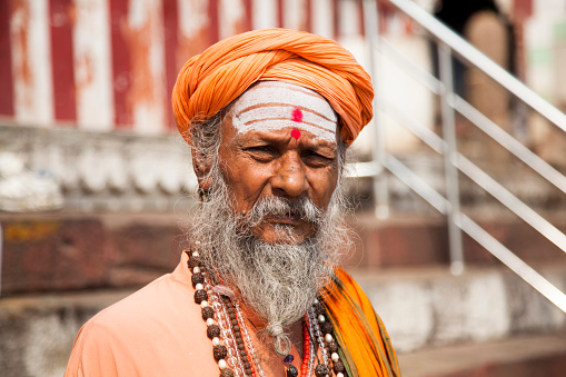 Varanasi - Ottobre 31,2016:  A long-bearded sadhu, or holy man sitting on the streets of Varanasi. This is one of the oldest inhabited cities in the world and also the holiest of the seven sacred cities in Hinduism and Jainism and so the most important pilgrimage place for hindus. Many ascetics in Varanasi like the one in the picture stay in visible places in the ghats decorated with images of the hindu gods to attract the attention and donations of pilgrims and tourists.