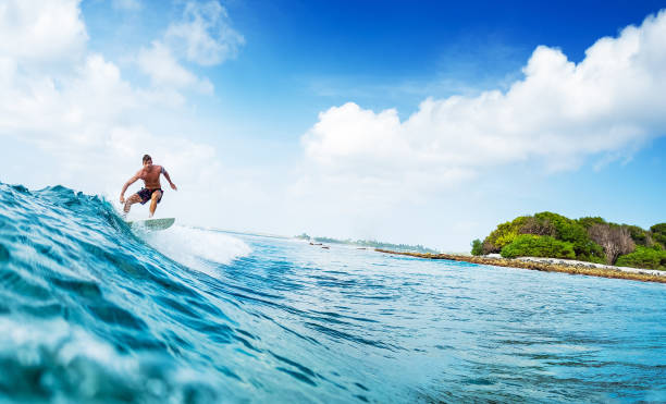 istock Young man surfs ocean wave in Maldives 1218732035