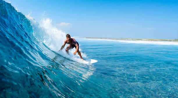 istock Young man surfs ocean wave in Maldives 1218732599