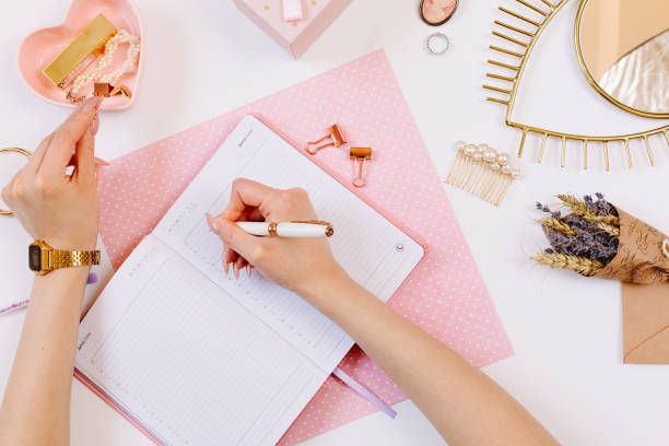 istock Girl keeps a diary and planning a day on stylish workplace. Female hand write in pink notebook. Women blog concept with pink notebook and golden watch. Flat lay style. 1218734890