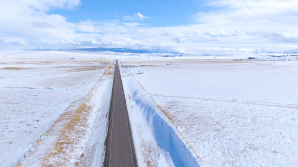 istock drone: flying along a long straight road leading through the wintry montana 1218736942