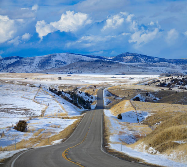 empty asphalt freeway runs across the beautiful snowy montana countryside in early spring. scenic vista of an interstate highway crossing the gorgeous rural landscape under the rocky mountains.