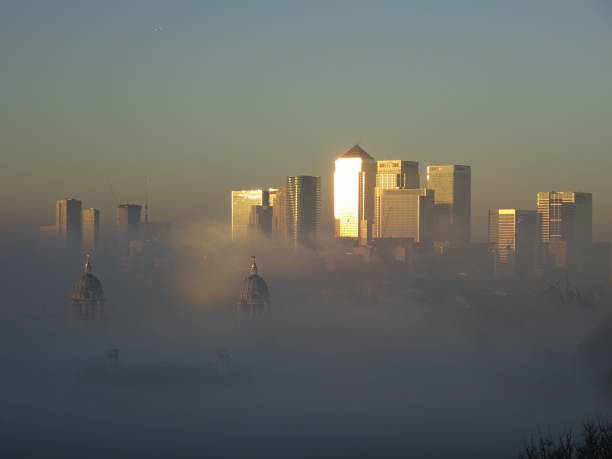 The Balance of Power Fog sinks to reveal the skysrapers of Canary Wharf behind the Royal Navy Collage and Queens House. queen's house stock pictures, royalty-free photos & images
