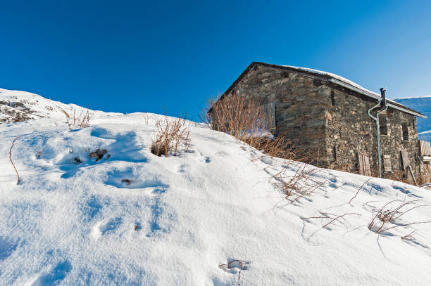 istock Panoramic view across snow covered slope on alpine mountain with small house 1218739631