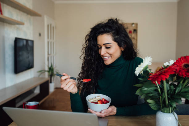 istock Young woman enjoying her breakfast and using laptop 1218741881
