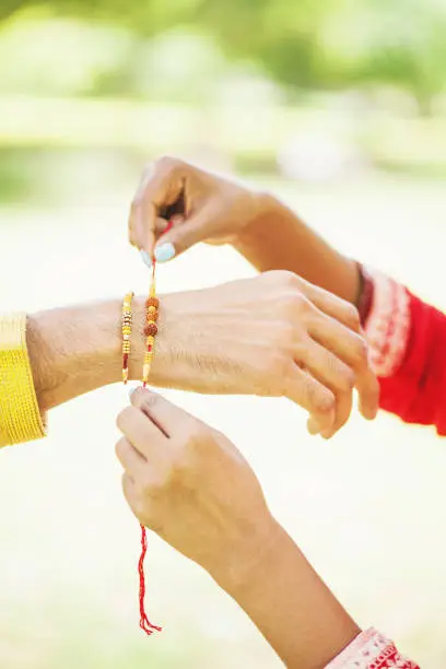 Closeup of hands photo: Indian woman tying rakhi on her brother's hand