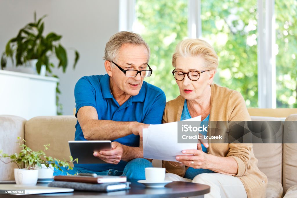 Retired couple watching bills and calculating monthly expenses Worried mature woman and man sitting on sofa in living room at home.  Senior couple working out a home budget Blue Stock Photo