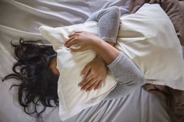 Ughhh this pain is killing me Portrait shot of sick woman lying in bed , covering her face with pillow, scared to have Coronavirus symptoms avoidance photos stock pictures, royalty-free photos & images