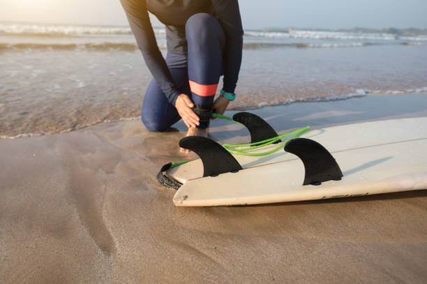 istock Woman surfer tying leg leash with surfboard on seaside reef 1218746450