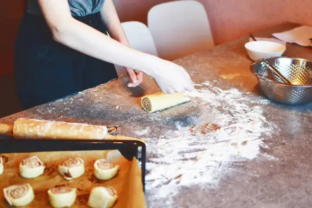 Girl makes homemade cinnamon buns sliced rolls of dough roll on grunge grey kitchen table. Tasty homemade snack concept.