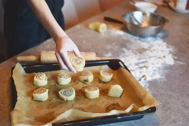 Girl makes homemade cinnamon buns sliced rolls of dough roll on grunge grey kitchen table. Tasty homemade snack concept.