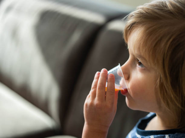 Small boy drinking syrup from a disposable cup dose. Cute little boy drinking cough syrup from a dose at home. Copy space. child liquid medicine stock pictures, royalty-free photos & images