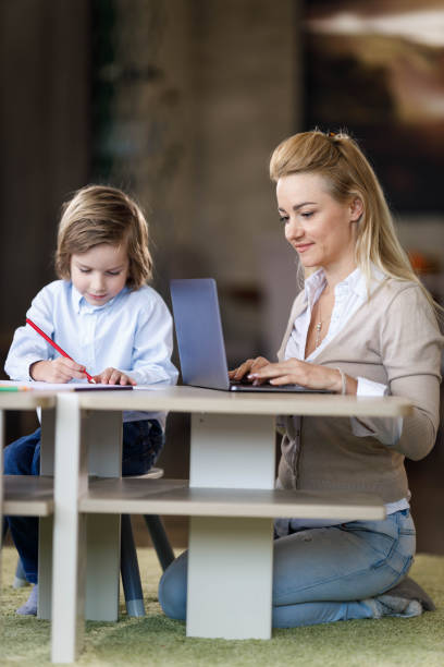 istock Working single mother using laptop while her son is coloring at home. 1218759393
