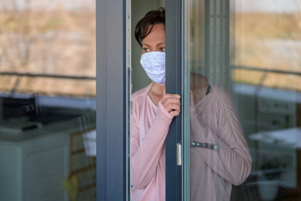 istock Woman wearing a face mask looking through window 1218759622