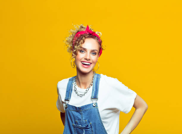 jeune femme gaie dans la tenue de modèle des années 80, verticale sur le fond jaune - salopette photos et images de collection